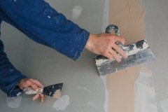 plasterer man works plastering two trowels on plasterboard in blue uniform